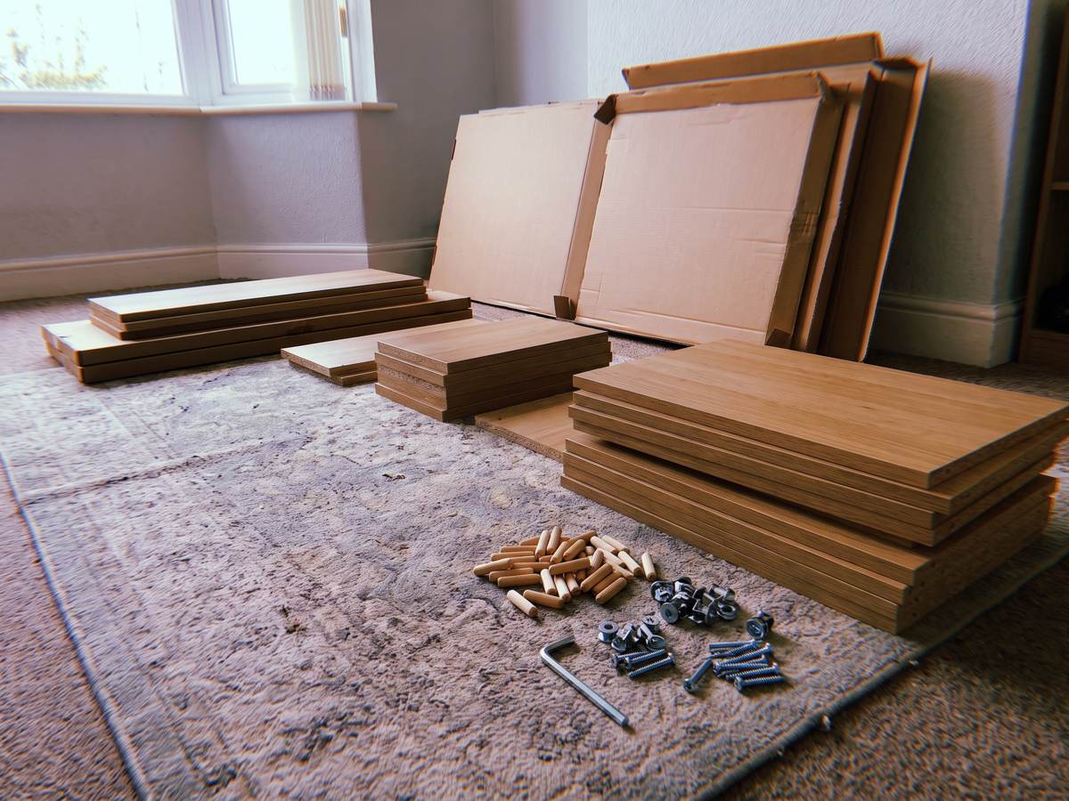 Flat pack furniture parts and fittings laid out in order on a living room floor