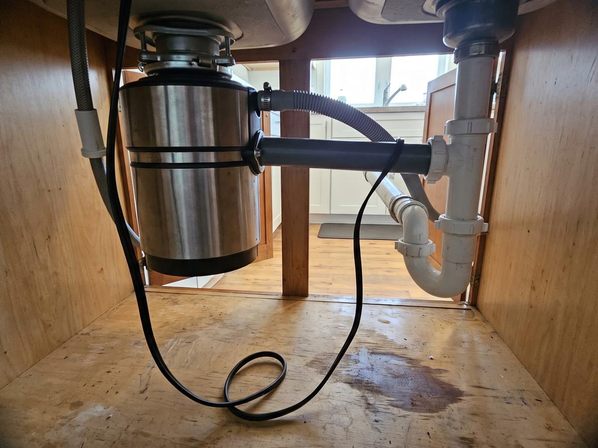 A stainless food waste disposer under a sink with its discharge tube running into the trap