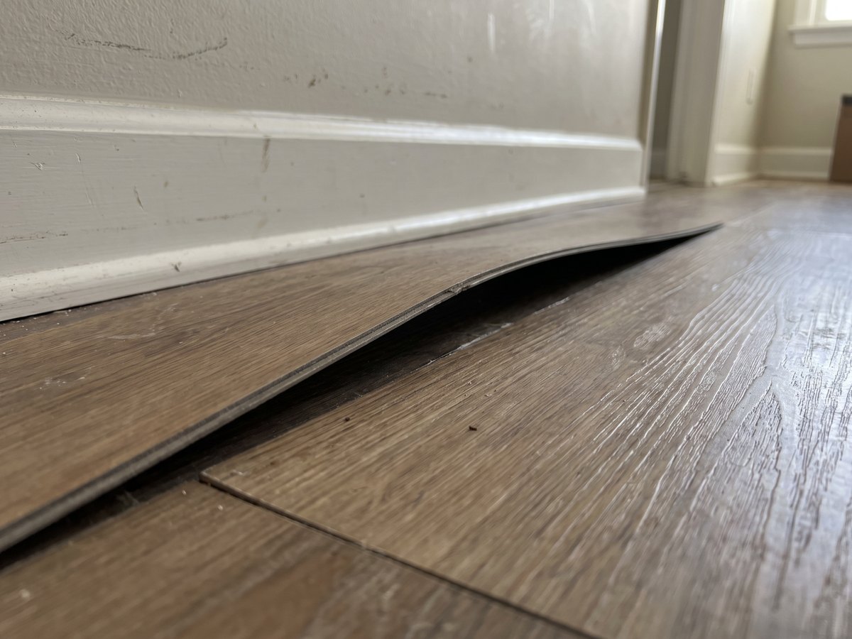 Two vinyl planks lifted apart at the seam with one edge curled