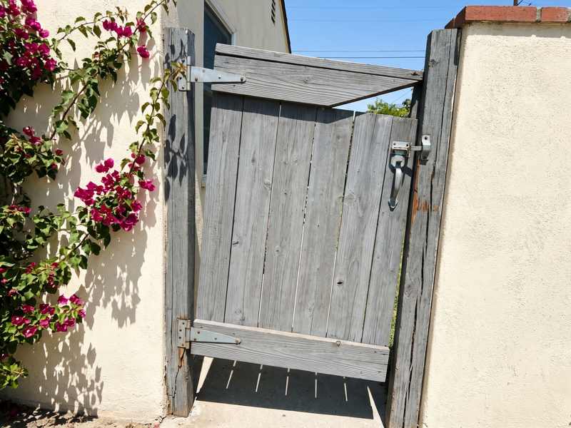 A wooden side gate hanging out of square on its hinges at a stucco wall