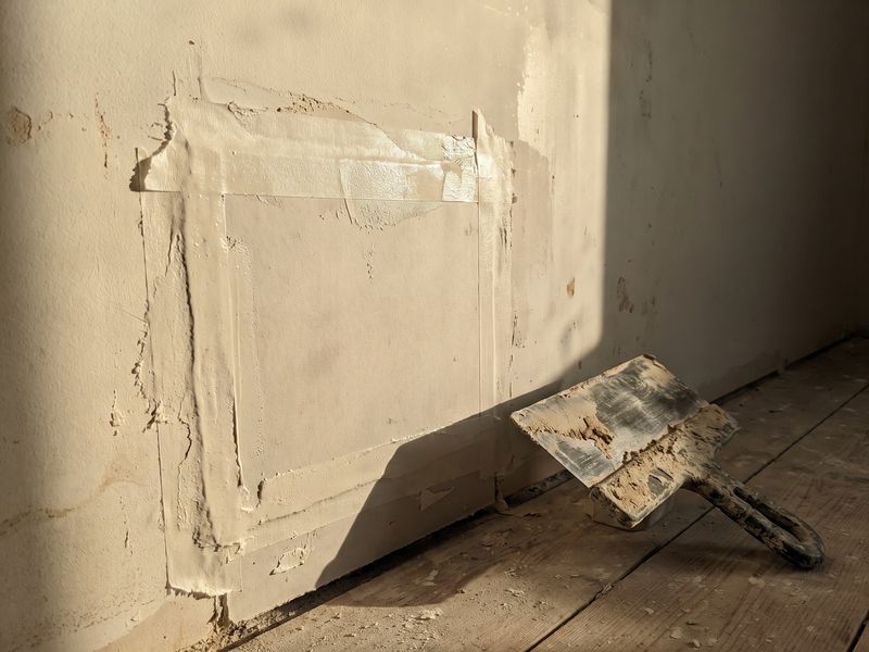 A drywall patch taped and bedded in compound, the feathered edge in raking light