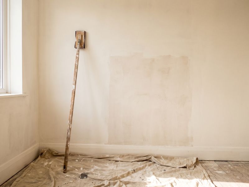 A sanding pole and dust sheet by a wall where a patch has been floated and primed