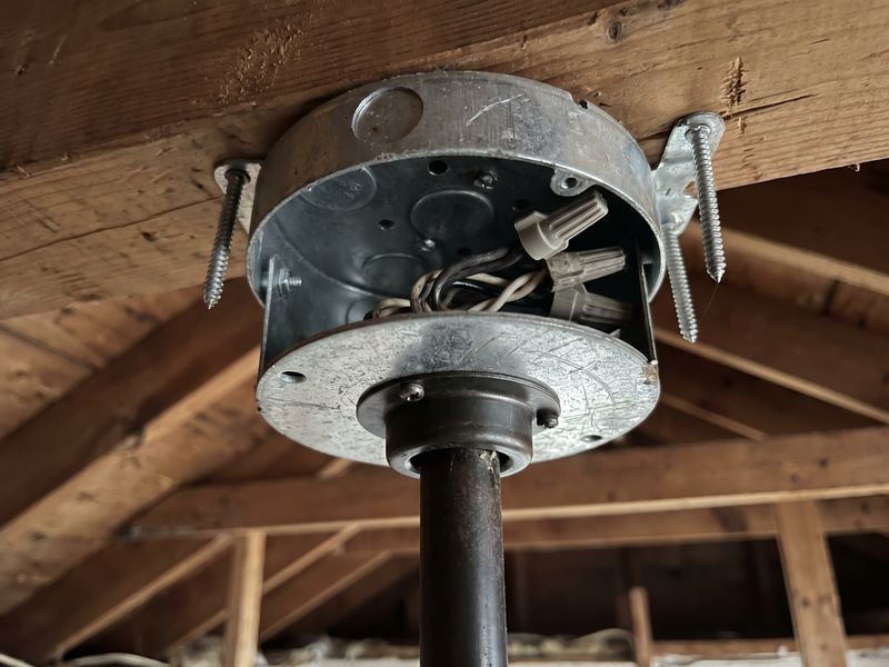 A fan-rated ceiling box screwed to a joist with the downrod collar below it