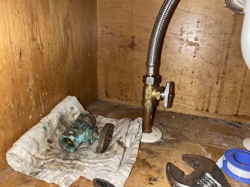 A braided supply line connected to a quarter-turn angle stop under a sink