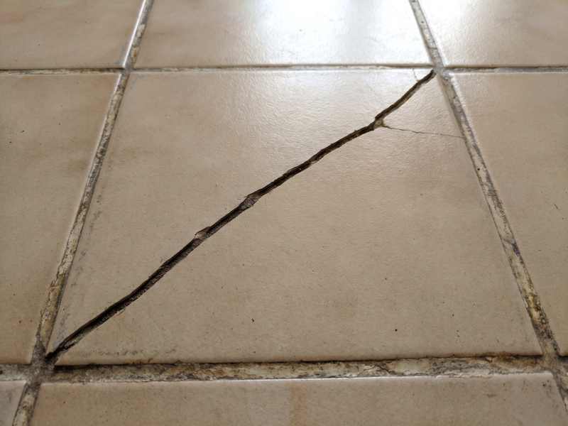 A cracked ceramic floor tile with dirt worked into the crack
