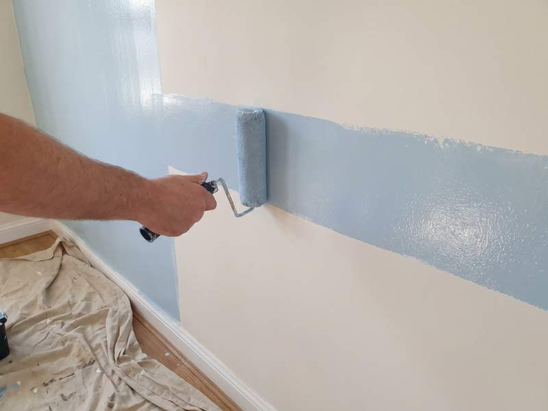 A roller laying fresh paint on a wall beside the older wall color