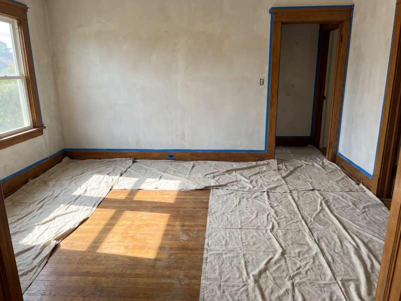 Masked baseboard and canvas dust sheets in an empty room ready for painting