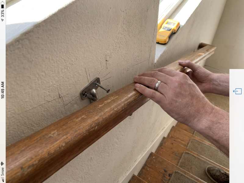 A stair handrail held against a wall while a bracket is fixed into framing