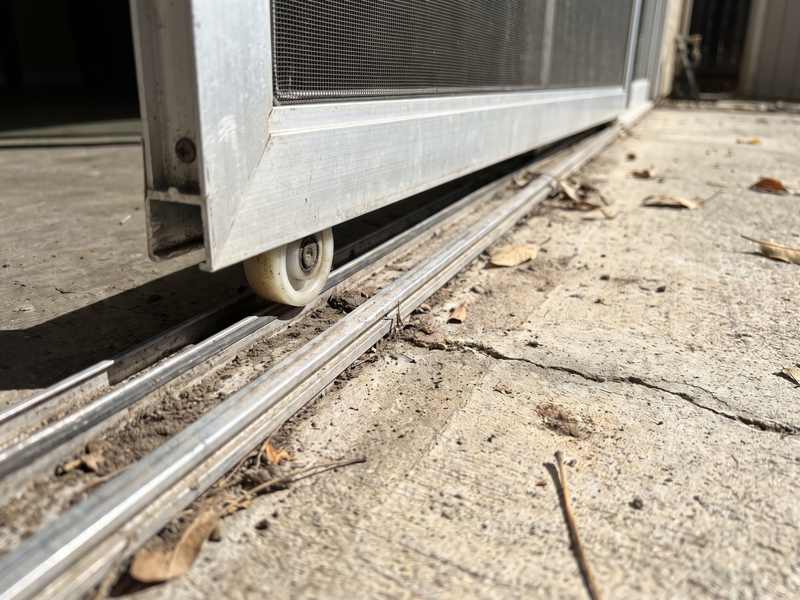 The bottom of a sliding screen door lifted off its track with grit in the channel