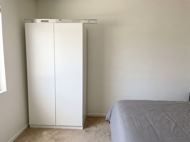 An assembled white wardrobe with the gap between its doors even from top to bottom and a level across its top