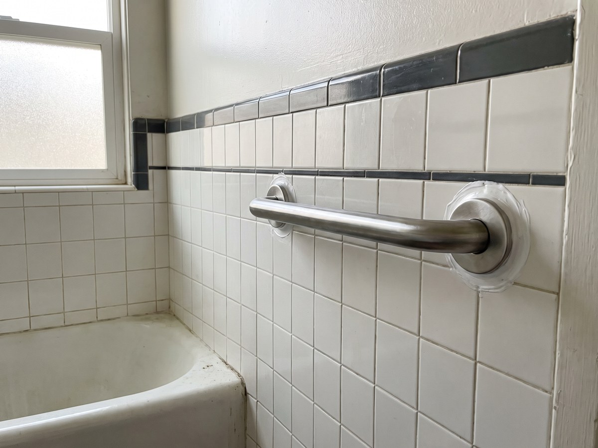 A stainless grab bar fitted on the tiled wall beside a bathtub