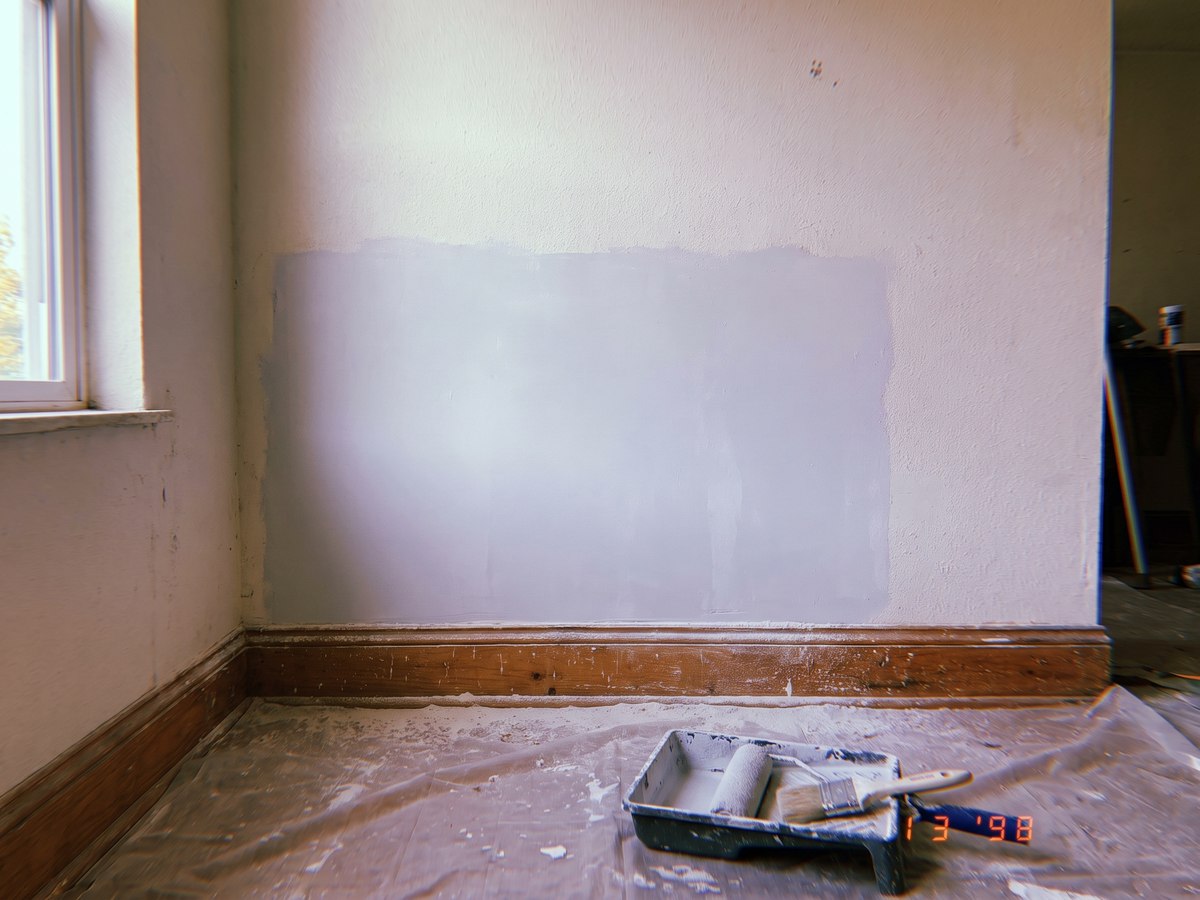 A wall repair sanded and spot primed, with a roller tray on a dust sheet below