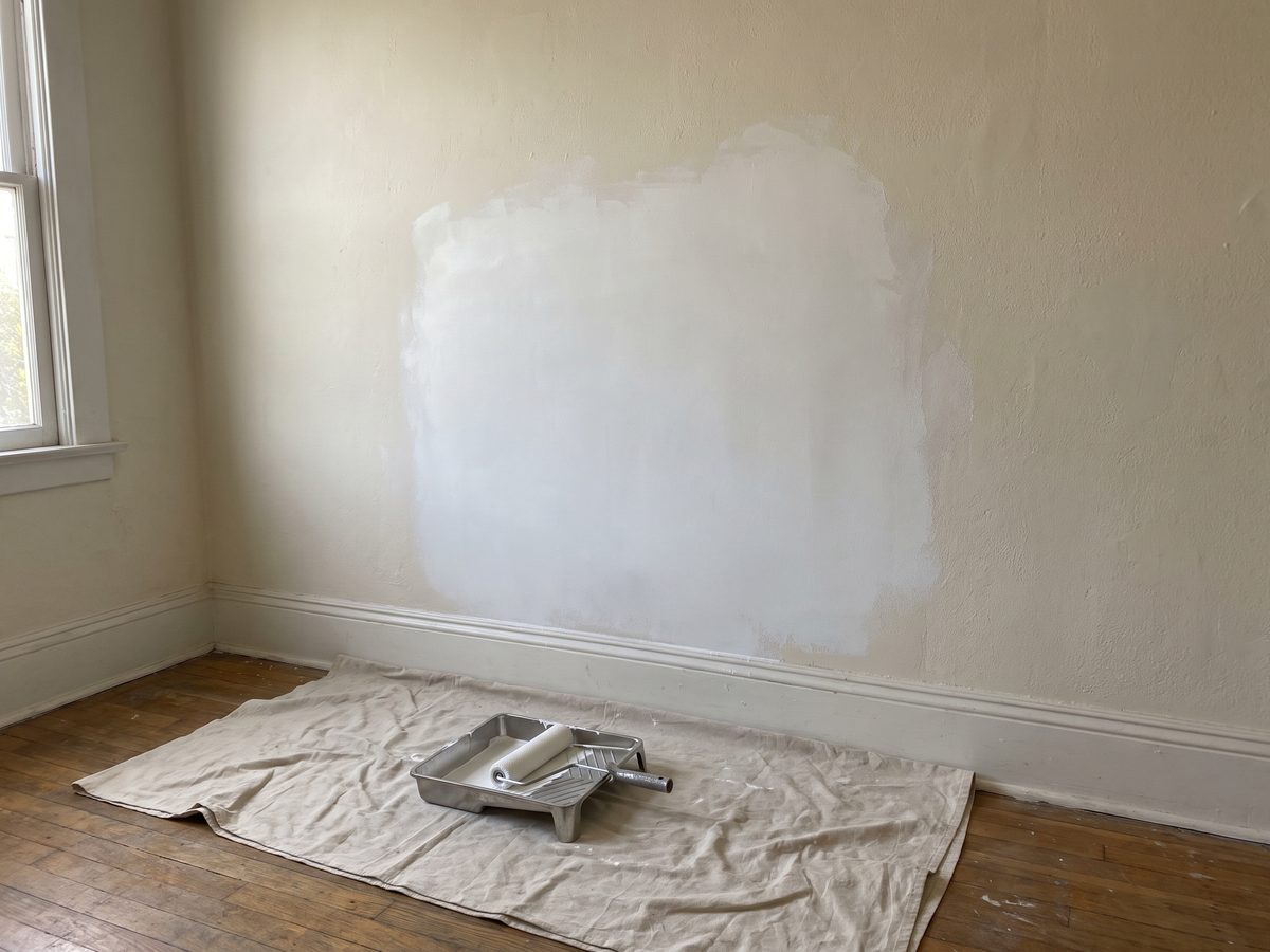 A wall repair sanded and spot primed, with a roller tray on a drop cloth below