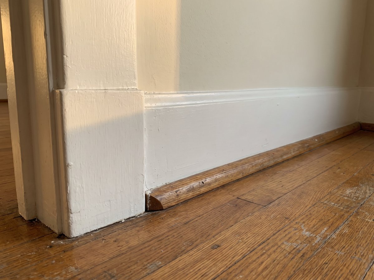 Painted baseboard meeting a door casing at a plinth block above an old oak floor