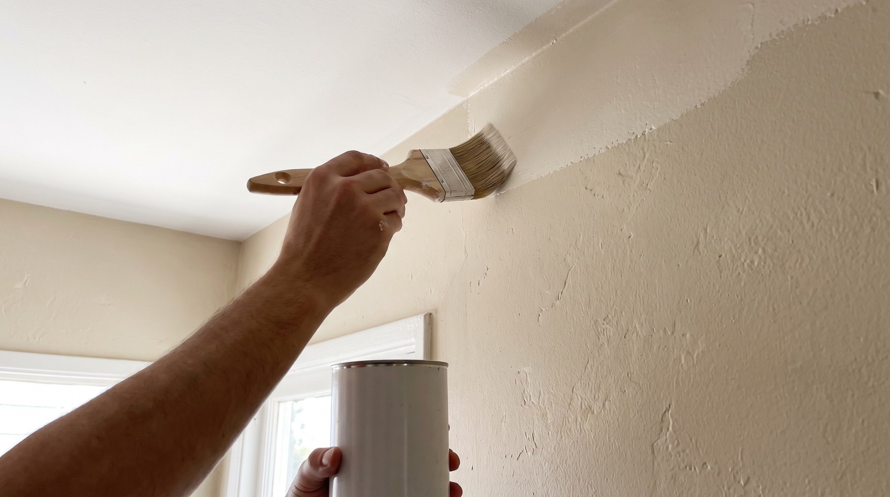 A hand cutting in with a sash brush along the line where a wall meets the ceiling