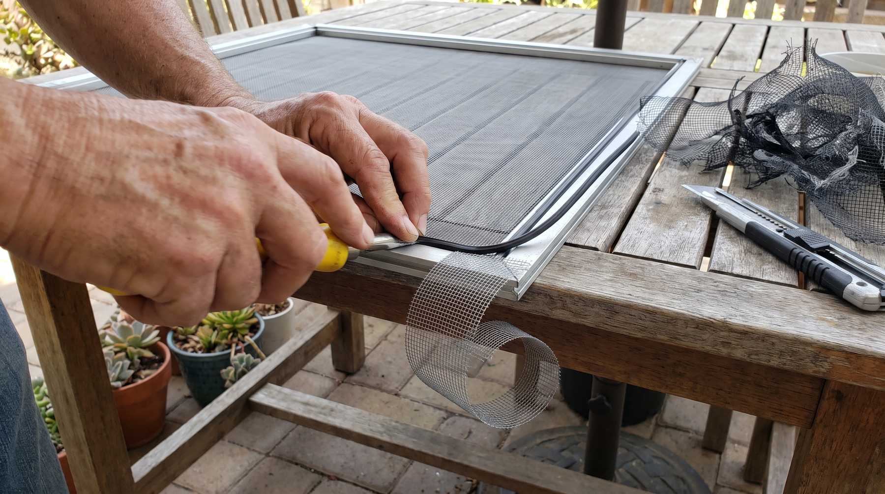 Hands rolling spline into the channel of an aluminum window screen frame